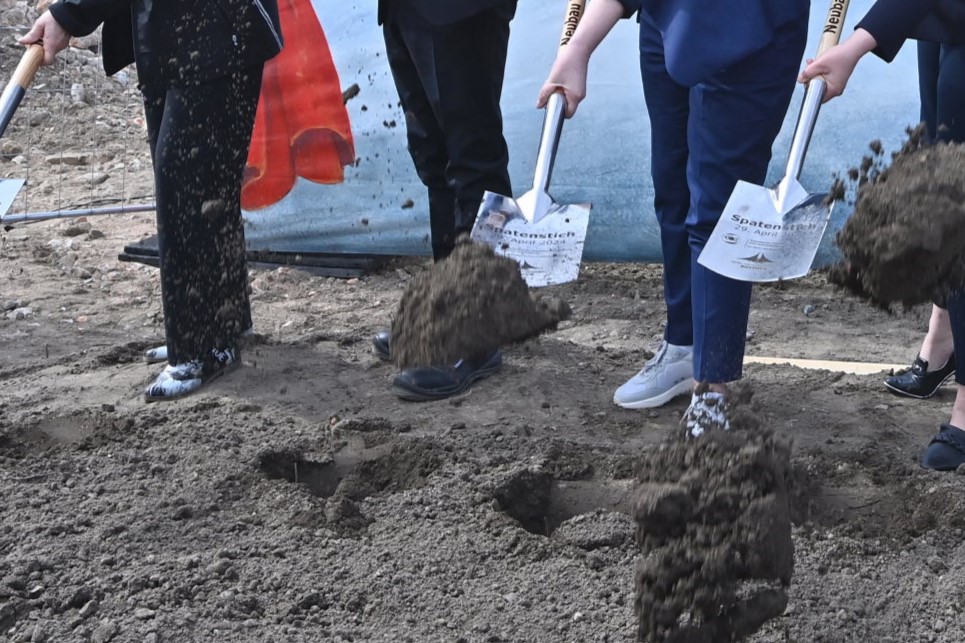 Personen beim Spatenstich mit individuell gravierten Spaten als feierlicher Baubeginn